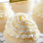 Pinterest image of a close-up shot of a vanilla cupcake piped with buttercream frosting resting on a cooling rack, with more cupcakes on the back.