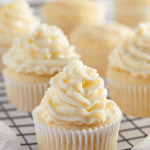 Pinterest image of a close-up shot of vanilla cupcakes piped with buttercream frosting resting on a cooling rack, with cupcakes with no frosting on the back.