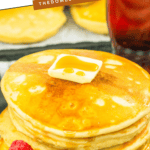 Pinterest image of a large stack of Cracker Barrel pancakes on a plate with a slice of butter dripped with syrup on top and berries on the side.