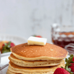 Pinterest image of a pat of butter sitting atop a stack of pancakes with whole strawberries on the plate beside it.