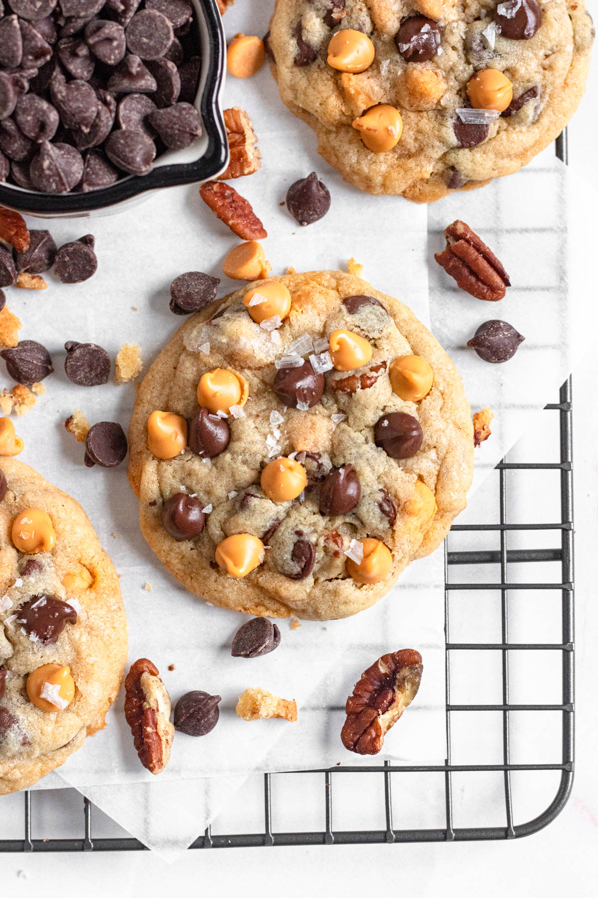 Baked cookie on a cooling rack surrounded by chocolate chips and pecans.