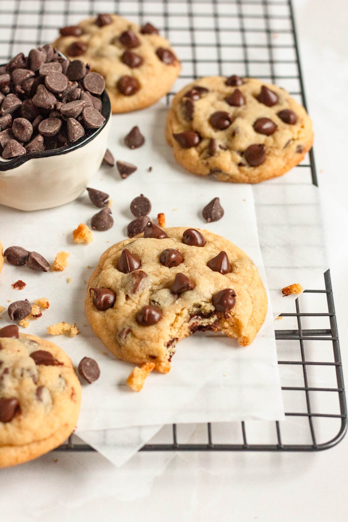 Chocolate chip cookie recipe with a bite taken out on a cooling rack surrounded by chocolate chips