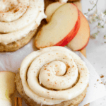 Pinterest image of applesauce cookies topped with brown butter cream cheese frosting piped over the top with apple slices and cinnamon sticks on the side.