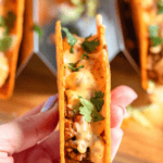 Pinterest image of a close-up shot of a hand holding Rotel Tacos filled with taco meat and cheese sauce.
