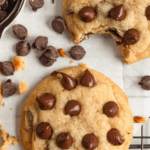 Pinterest image of an overhead shot of a chocolate chip cookie on a cooling rack with baking paper, cookie crumbs, chocolate chips, and two more cookies on the side.