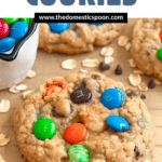 Pinterest image of monster cookies with oats and chocolate chips on the side on a parchment-lined baking rack.