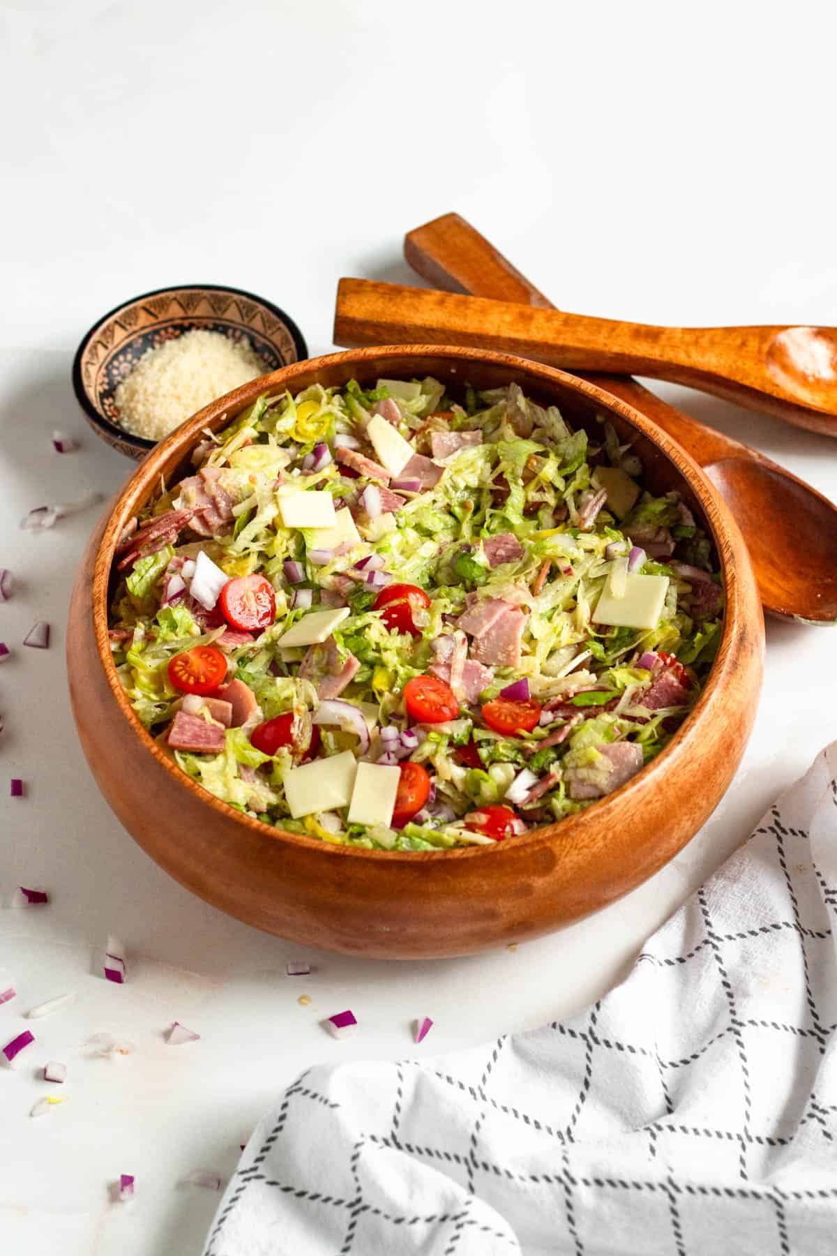 Grinder Salad in a wooden bowl surrounded by cheese, serving utensils, and a napkin