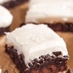 Pinterest image of a close-up of a rich, fudgy brownie topped with thick cream cheese frosting over the top and chocolate chips garnished around it.
