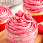 Pinterest image of an overhead shot of raspberry cream cheese frosting piped into a small glass jar with fresh raspberries garnished around the bottom.