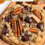 Pinterest image of a close-up shot of one chocolate chip pecan cookie with sea salt on top, with pecans and chocolate chips around it.