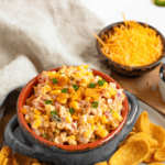 Pinterest image of a bowl of Corn Fritos Dip resting on a plate filled with Frito corn chips to be used as dippers, with a small bowl of cheese on the back.