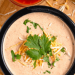 Pinterest image of a top-view shot of the Mexicali dip in a small dish with cilantro and shredded cheese, garnished on top with a small bowl of salsa and tortilla chips around the dip.