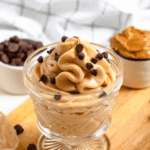 Pinterest image of a shot of Peanut Butter Mousse piped into a small glass jar with chocolate chips sprinkled on top and some scattered in front of the dessert with the piping bag laying to the side.