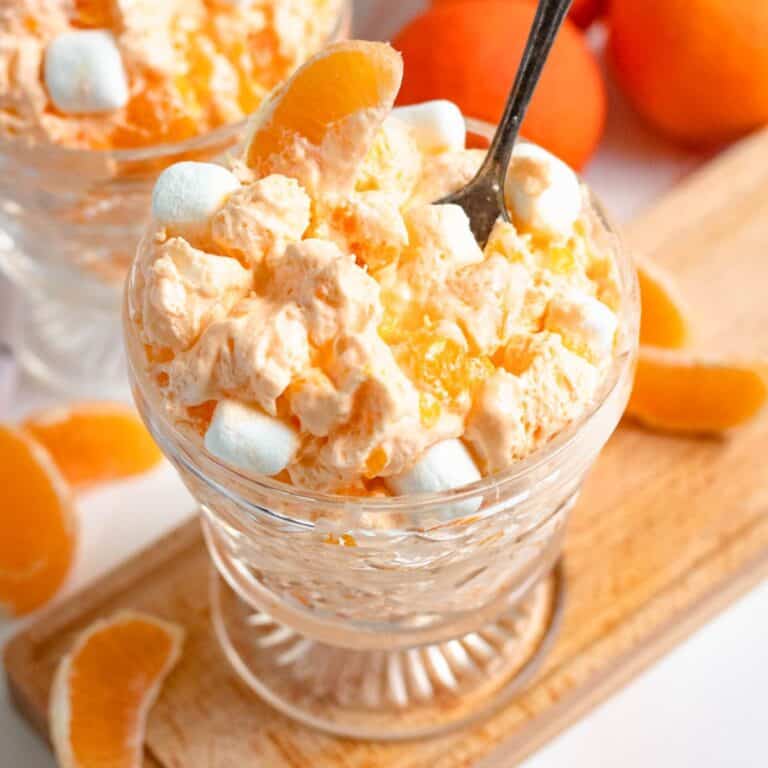Close up of a glass filled with orange dreamsicle salad and a spoon resting in the mixture.
