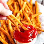 Pinterest image of a hand dipping air fried Checkers' fries in a heaping mini bowl of ketchup.