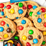 Pinterest image of an overhead shot of a stack of Peanut Butter M&M Cookies on a plate with a tiny bowl of M&Ms.