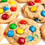 Pinterest image of a close-up shot of Peanut Butter M&M Cookies on parchment paper.