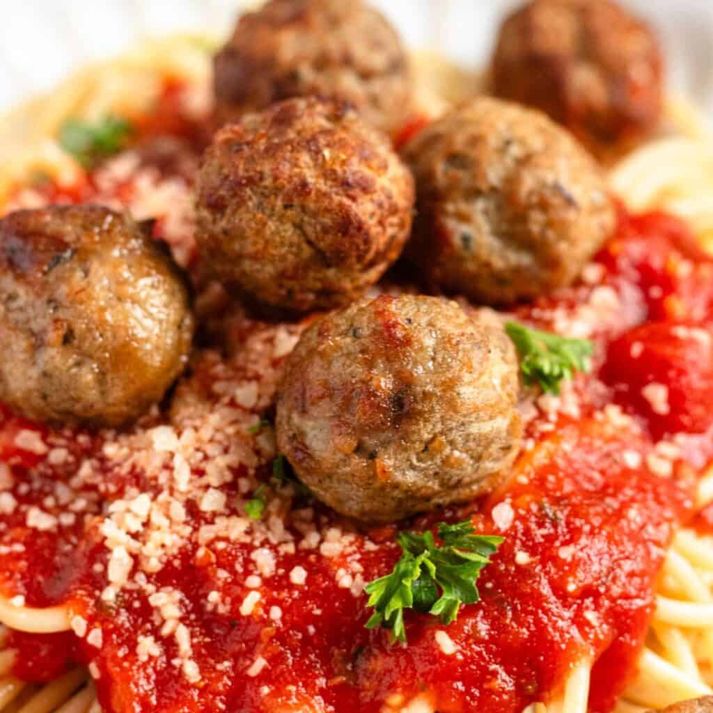 Meatballs prepared in the air fryer on top of a bed of spaghetti sprinkled with parmesan cheese.