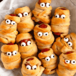 Pinterest image of a serving bowl with mummy pigs in a blanket with candy eyes.
