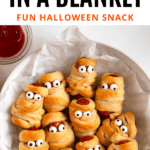 Pinterest image of a serving bowl with mummy pigs in a blanket with candy eyes.