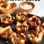 Pinterest image of a plate of golden, flaky brie puff pastry bites filled with brie, cranberry jam, and walnuts, garnished with fresh rosemary and sea salt.