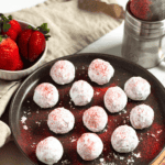 Pinterest image of a top-view shot of a plate of strawberry truffles coated in powdered sugar and dusted with freeze-dried strawberry powder, surrounded by fresh strawberries.