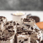 Pinterest image of a stack of creamy Oreo fudge cubes topped with crushed Oreos sits on a plate with parchment paper.