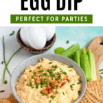 Pinterest image of the top view of creamy deviled egg dip served with crackers, celery sticks, and baby carrots on a wooden board.
