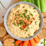 Pinterest image of the top view of creamy deviled egg dip served with crackers, celery sticks, and baby carrots on a wooden board.