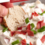 Pinterest image of a close-up shot of a creamy bagel dip topped with green onions and dried beef, with a hand dipping a sesame bagel slice into it.
