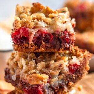 A close-up of stacked cherry bars filled with coconut, chocolate chips, walnuts, and a graham cracker crust.