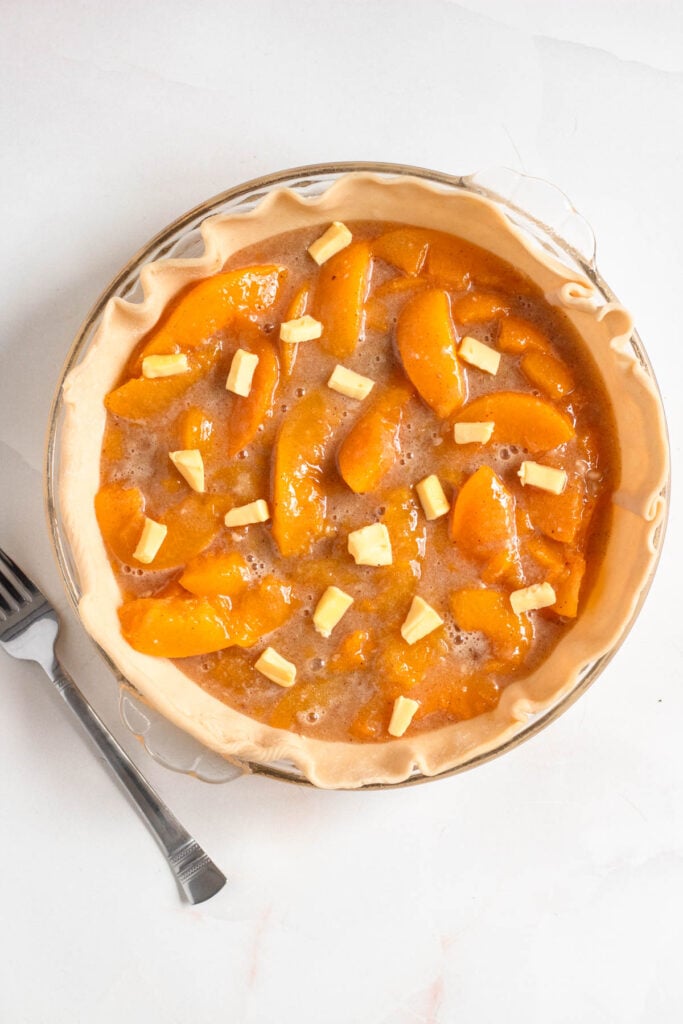 Peach pie filling was poured into the prepared pie crust and topped with small pieces of butter.