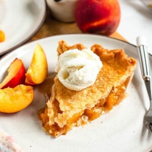 A slice of juicy peach pie with vanilla ice cream and peach slices on the side.