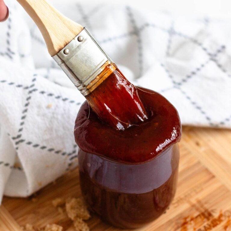 Thick 3 ingredient barbecue sauce coats a basting brush over a jar, with brown sugar scattered on a wooden board