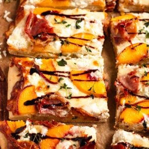 A golden peach pizza topped with prosciutto, goat cheese, thyme, and a drizzle of balsamic glaze.