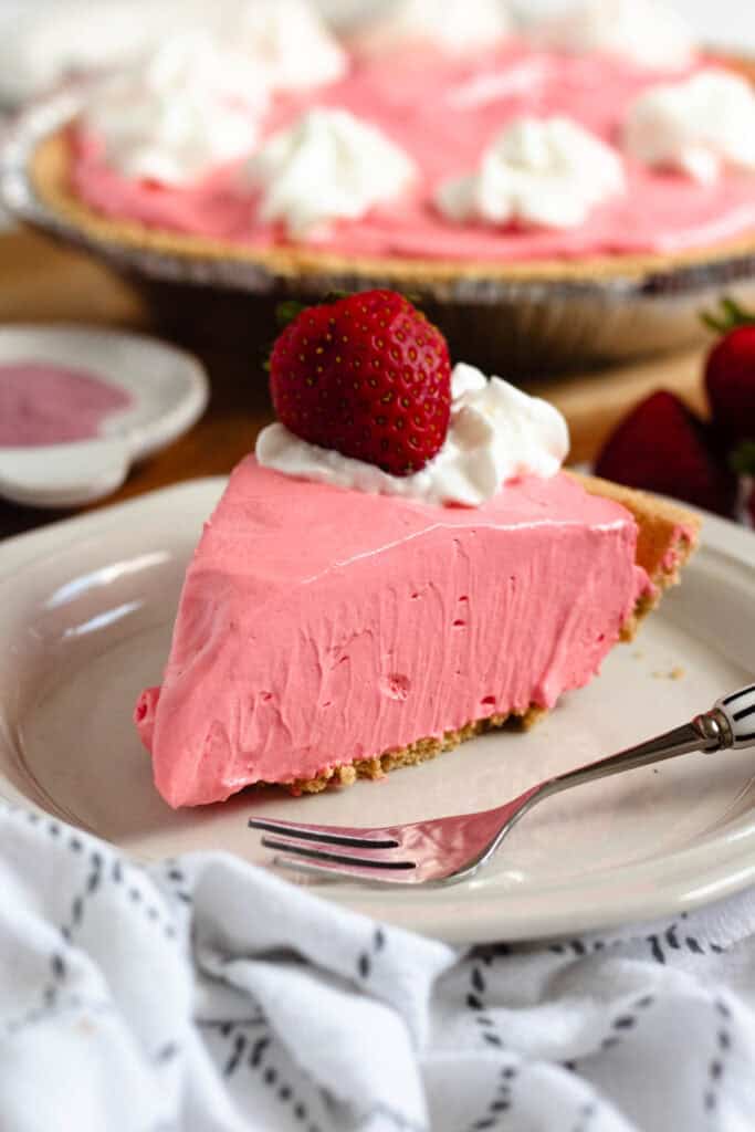 A slice Kool Aid pie topped with whipped cream and a fresh strawberry on a white plate.