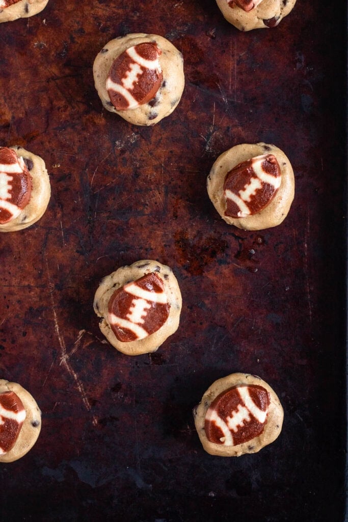 Unbaked football cookie placed on top of chocolate chip cookie dough ball.