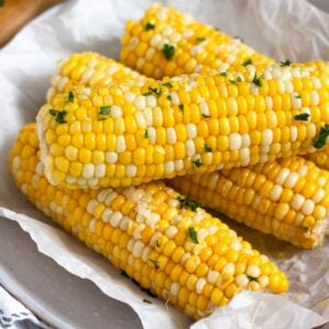 Freshly cooked corn on the cob topped with butter, and salt on a plate.