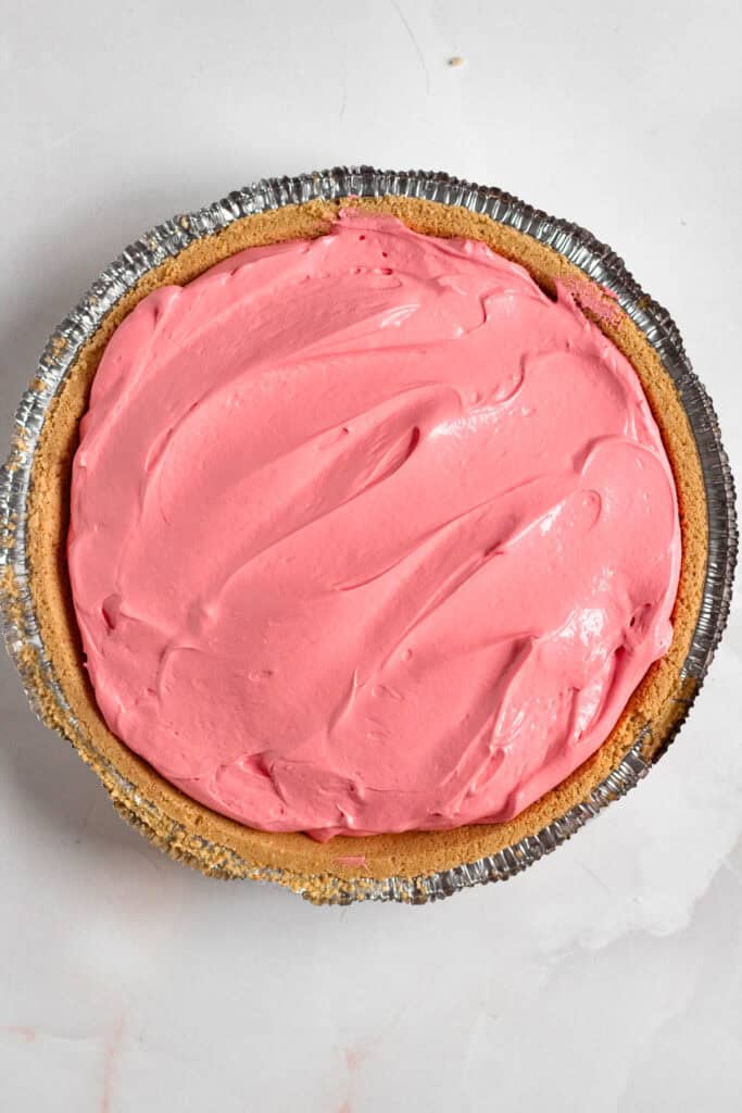 Kool-Aid pie filling being poured into a graham cracker crust.