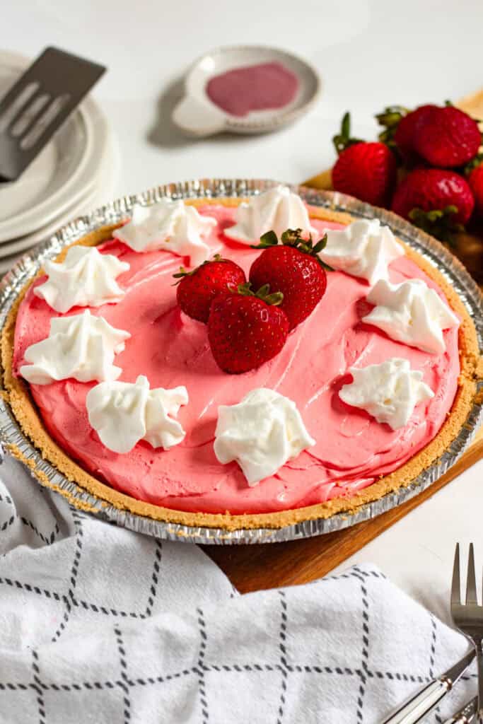 A whole Kool Aid pie with whipped cream dollops, and fresh strawberries on top in a graham cracker crust.