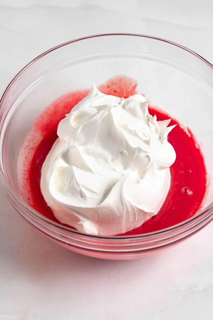 A bowl of Kool Aid pie mixture with Cool Whip being gently folded in.