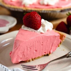 A slice Kool-Aid pie topped with whipped cream and a fresh strawberry on a white plate.