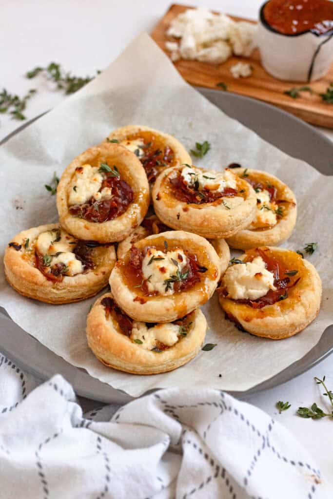 A plate of delicious Goat Cheese Appetizers with flaky Puff Pastry and apricot jam topped with herbs.