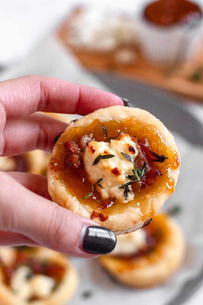 A hand holding a delicious Goat Cheese Appetizer with flaky Puff Pastry and apricot jam.