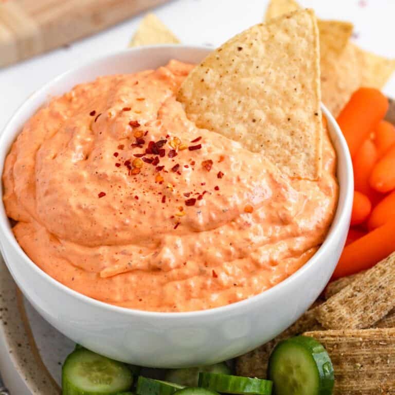 Creamy roasted red pepper dip served with tortilla chips, cucumbers, and veggies on a platter.