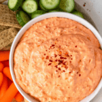Pinterest image of a top-view shot of the creamy roasted red pepper dip served with tortilla chips, cucumbers, and veggies on a platter.