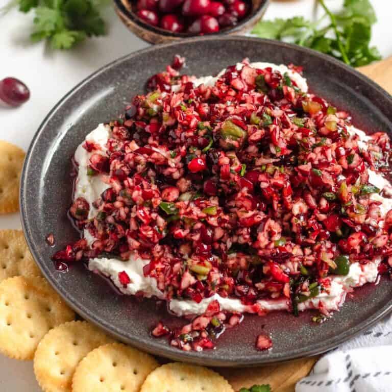 A vibrant cranberry salsa spread over creamy cheese and served with crackers on a plate.