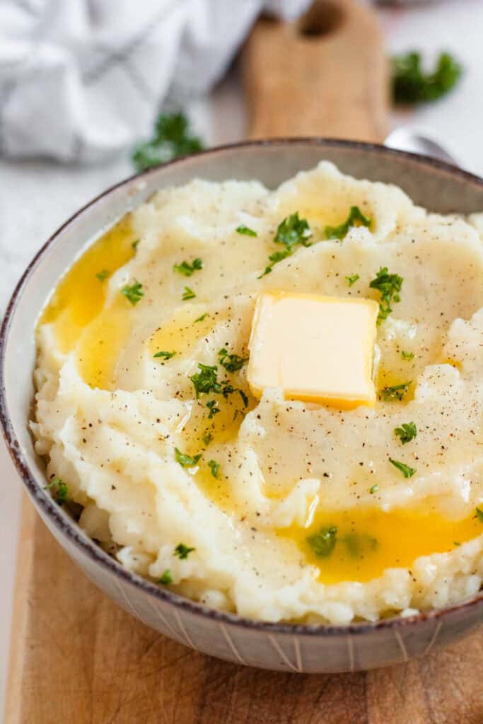 A bowl of creamy mashed potatoes topped with melted butter, black pepper, and fresh parsley.