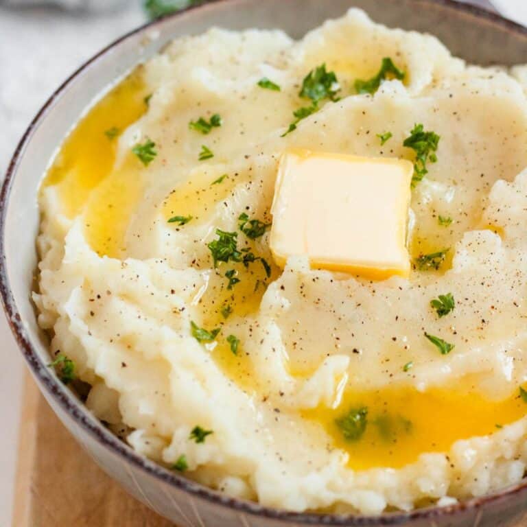 A bowl of creamy mashed potatoes topped with melted butter, black pepper, and fresh parsley.