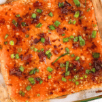 Pinterest image of a top-view shot of Captain Rodney’s Dip topped with crispy bacon and green onions in a glass dish with crackers and parsley on the side.
